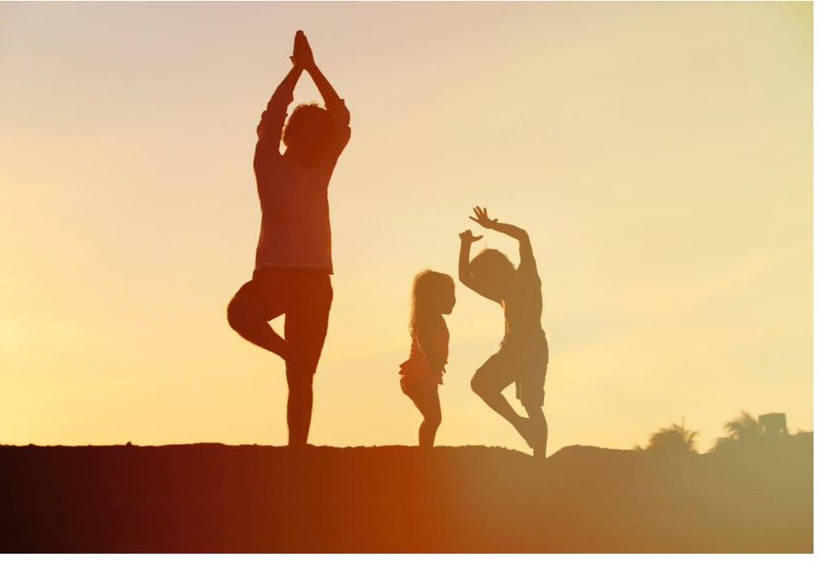 Elternteil und Kind üben gemeinsam Yoga im Sonnenuntergang