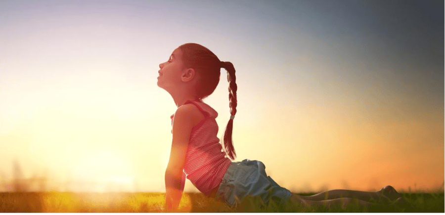 Mädchen übt Kinderyoga auf der Wiese im Abendlicht