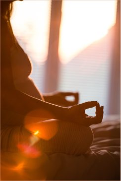 Schwangere Frau sitzt im Meditationssitz im warmen Abendlicht